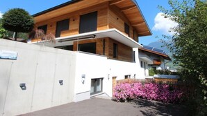 Una moderna casa a due piani con facciata in legno, esterno bianco e un piccolo giardino con fiori rosa.