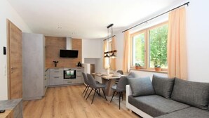 Un soggiorno moderno con un divano grigio, un'area pranzo con tavolo e sedie, e una cucina con una TV sopra il bancone.