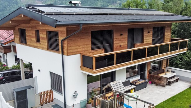 Una moderna casa a due piani con un balcone, un'area giochi e un tetto con pannelli solari.