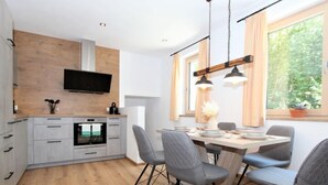 Una cucina moderna con forno integrato, TV montata sopra il bancone e zona pranzo con tavolo in legno e sedie grigie.