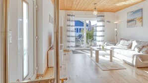 Ein modernes Wohnzimmer mit Holzbalkendecke, einer Couch, einem Couchtisch und Blick durch eine Glastür auf einen Außenbereich.
