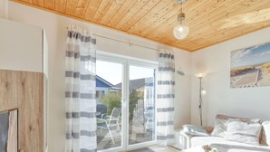 Ein modernes Wohnzimmer mit Holzboden, einem großen Schiebeglastür, einer Couch, einem Couchtisch und einem Fernseher.