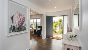 Un couloir moderne agrémenté d’une œuvre d’art encadrée, d’un fauteuil bleu foncé et offrant une vue sur un jardin par une porte ouverte.
