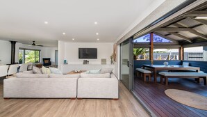 Un salon moderne avec un canapé, un téléviseur et un coin repas comprenant une table et des bancs.