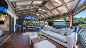 Un espace de vie extérieur abrité, doté d’une terrasse en bois, d’un canapé, d’une table et d’un barbecue.