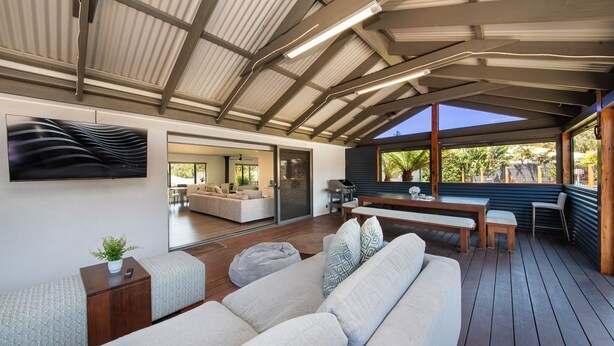 Un intérieur moderne avec une terrasse en bois, un canapé, une table à manger et une grande fenêtre donnant sur l’extérieur.