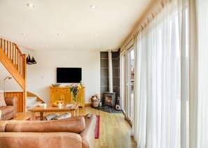A living room with a sofa, coffee table, TV, fireplace, and a staircase. - Stunning lodge built over the edge of the lake. (Anglesey)