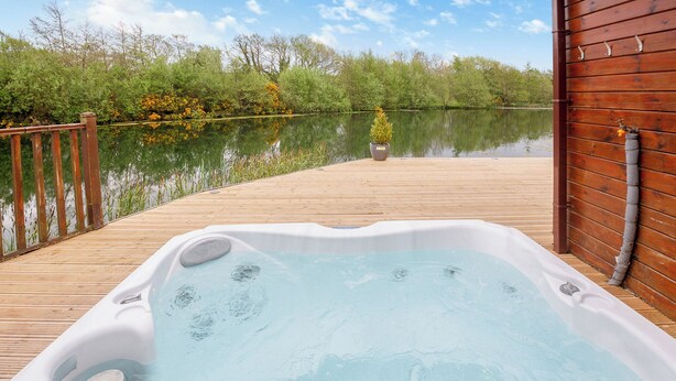 Ein Whirlpool auf einer Holzterrasse mit Blick auf einen stillen See und Bäume.