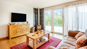 Una sala de estar con televisor, aparador de madera, chimenea, sofá y ventanas amplias.