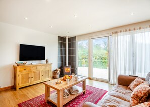 A living room with a TV, wooden cabinet, fireplace, sofa, and large windows. - Stunning lodge built over the edge of the lake. (Anglesey)