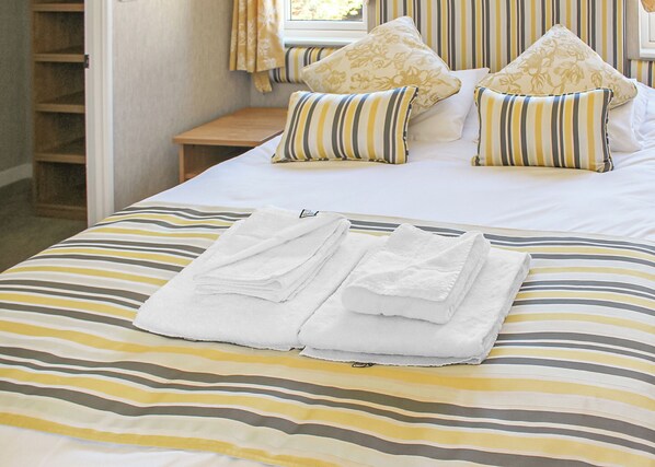 A neatly made bed with striped bedding, pillows with floral patterns, and a stack of white towels.