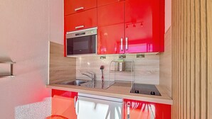 A compact kitchen with red cabinets, a stainless steel sink, and a built-in oven. - Renovated bright studio, ski-in/ski-out, balcony, sleeps 3 (Les Menuires)