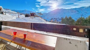 A wooden bench with two red cups, overlooking a snowy mountain landscape with a ski lift and a clear blue sky. - Renovated bright studio, ski-in/ski-out, balcony, sleeps 3 (Les Menuires)