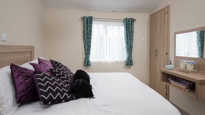 A bedroom with a bed, pillows, a nightstand, a mirror, and a window with curtains.