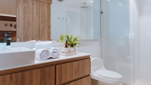 Un baño moderno con tocador de madera, lavamanos blanco y cabina de ducha de vidrio.