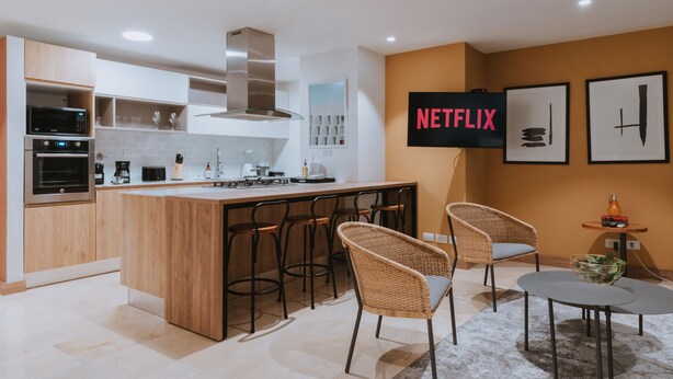 Una cocina moderna con una isla central, taburetes de bar y un comedor con una mesa pequeña y sillas.