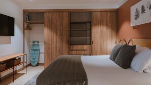 Un dormitorio con una cama, un armario de madera, un televisor, un cabecero de mimbre y una obra de arte colgada en la pared.