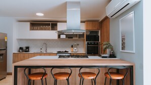 A modern kitchen with a central island, bar stools, wooden cabinets, a stainless steel range hood, and a built-in microwave.