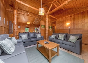 A log cabin interior with two gray sofas, a wooden coffee table, and a hanging light fixture.