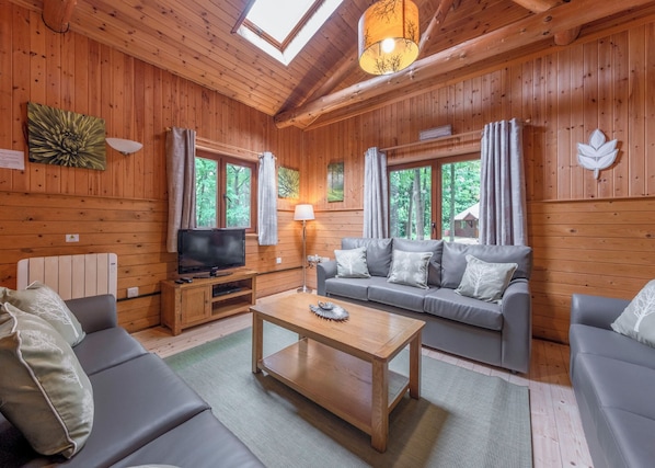A wooden cabin interior with a sofa, a coffee table, a TV, and a lamp.