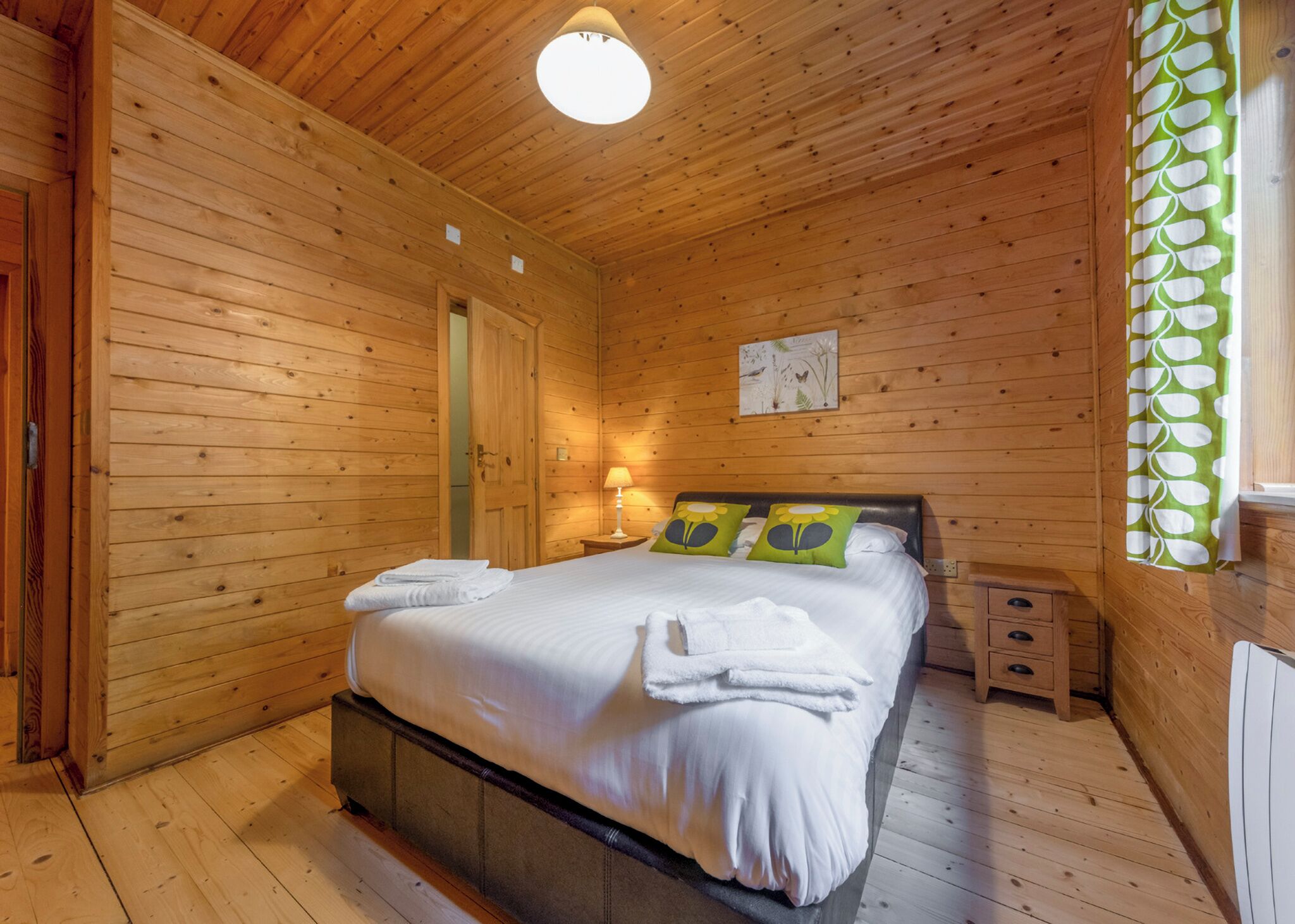 Een houten kamer met een bed, een nachtkastje en een wandlamp.