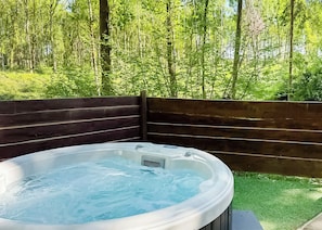 A hot tub surrounded by a wooden fence with a forest view.