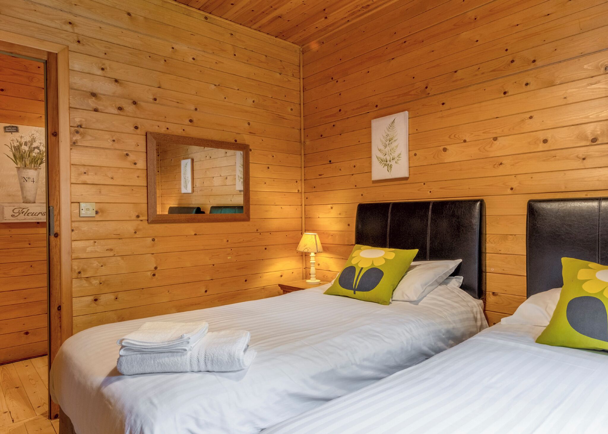 A wooden cabin room with two beds, a mirror, and a wall-mounted picture.
