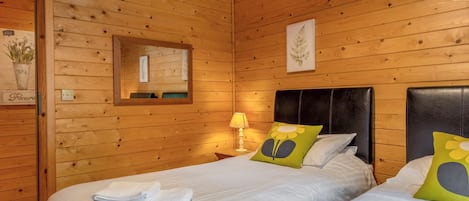 Una habitación de cabaña de madera con dos camas, un espejo y un cuadro colgado en la pared.