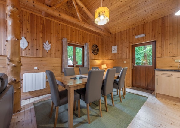 A wooden cabin interior with a dining table, chairs, a lamp, and a window.