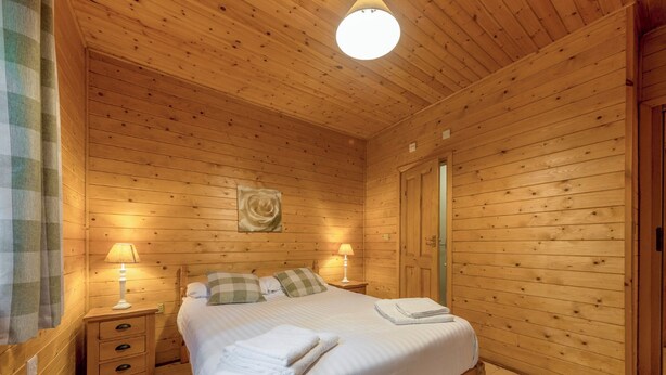 Ein Schlafzimmer mit Holzwänden, einem Bett, zwei Nachttischlampen, einem Nachttisch, einer Kommode und einer Tür.