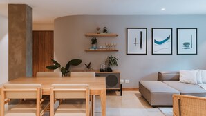 Ein modernes Wohnzimmer mit Essbereich, ausgestattet mit einem Holztisch und Stühlen, einem grauen Sofa und einem Konsolentisch mit Dekoration und gerahmten Kunstwerken.