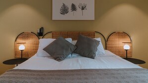 Ein ordentlich bezogenes Bett mit zwei Kissen, ein gerahmtes Pflanzenbild darüber und je eine Wandlampe auf beiden Seiten.