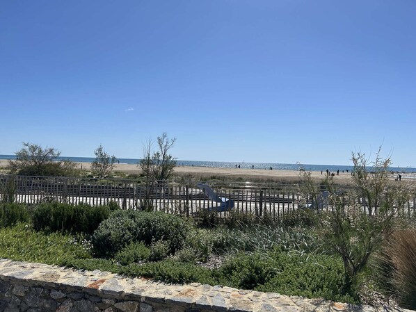 Un paysage côtier avec un mur de pierres, une végétation clairsemée et un ciel bleu dégagé.