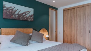 Un dormitorio con cama, almohadas, una obra de arte en la pared, un armario de madera y un cabecero de mimbre.