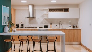 Una cocina moderna con una isla central, taburetes de bar, armarios de madera y diversos electrodomésticos.