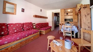 Ein gemütliches Wohnzimmer mit einem roten Sofa, einem Holzespeisetisch mit Stühlen und einem durch eine offene Tür einsehbarer Küchenbereich.