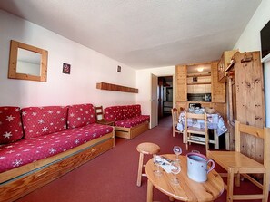 Ein gemütliches Wohnzimmer mit einem roten Sofa, einem Holzespeisetisch mit Stühlen und einem durch eine offene Tür einsehbarer Küchenbereich.