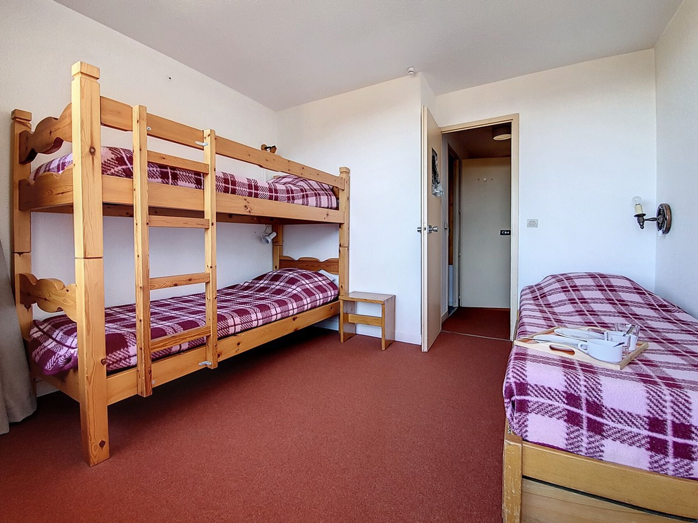 Ein Zimmer mit Etagenbetten, einem Einzelbett, einem kleinen Tisch und einer Tür zu einem weiteren Raum.