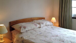 A bed with floral bedding, a wooden headboard, two bedside lamps, and a window with curtains. - 2 bedroom accommodation in Wroxham, Norfolk Broads (Wroxham, Norfolk Broads)