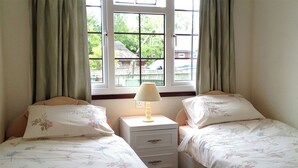 A bedroom with two beds, a nightstand with a lamp, and a window with curtains. - 2 bedroom accommodation in Wroxham, Norfolk Broads (Wroxham, Norfolk Broads)