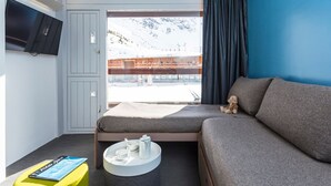 Une chambre d’hôtel moderne équipée d’un lit, d’un canapé, d’un téléviseur fixé au mur et d’une fenêtre donnant sur une montagne enneigée.