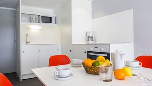 Une cuisine moderne avec des meubles blancs, un four à micro-ondes, une machine à café et un panier de fruits posé sur le plan de travail.