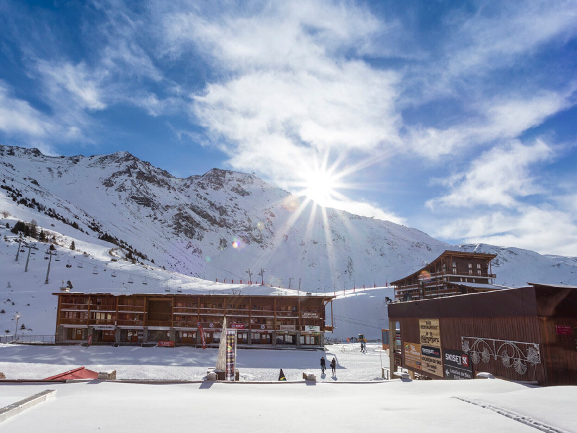 Un complejo turístico en la montaña cubierto de nieve, con un telesilla y un edificio de madera con telesilla, y un cartel que dice 'SKISET'.