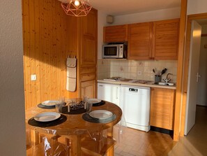Uma cozinha compacta com armários de madeira, micro-ondas, lava-louças e uma mesa de jantar posta para quatro pessoas.
