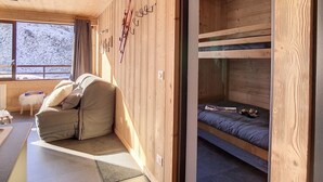 En hyggelig hytte med træpaneler, køjeseng, sofa og et stort vindue med udsigt til et sneklædt landskab.