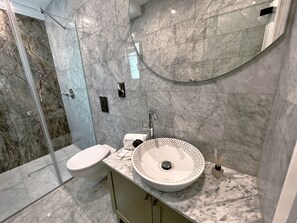 A modern bathroom with a marble sink, toilet, and shower. - Indepenence Emerald-1 Bedroom Apartment (Valletta)