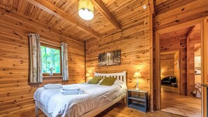 Une chambre dans une cabane en bois, avec un lit, une table de chevet et une fenêtre avec des rideaux.