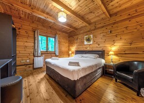 A wooden cabin bedroom with a bed, bedside lamp, and a window. - Woodland Hawthorn Lodge (Ellesmere)