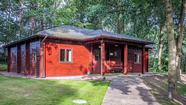 Une cabane en bois avec un porche, un chemin de pierres et une cour verdoyante entourée d’arbres.