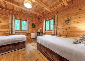 A cabin with two beds, wooden walls, a radiator, and a window with curtains. - Woodland Hawthorn Lodge (Ellesmere)